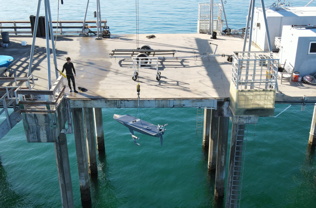 A seasats autonomous surface vehicle being lowered from a dock using a crane