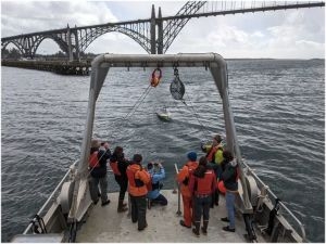 A group of people stands on the back of a larger vessel taking pictures of a Lightfish surface vehicle in the water.