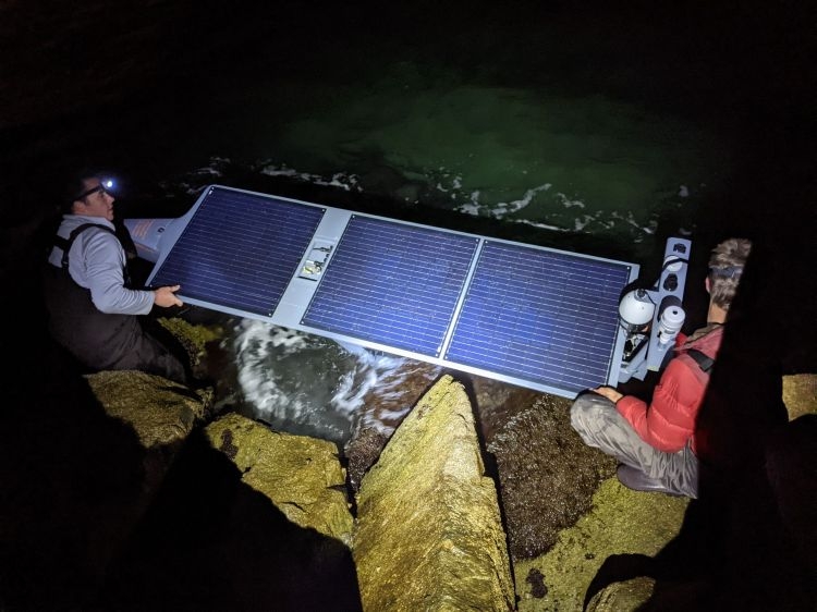 Two people launching a Seasats ASV from a rocky shoreline at night